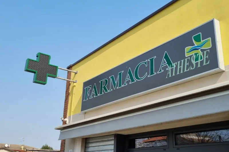 Insegna FARMACIA ATHESTE e croce a LED su una facciata gialla