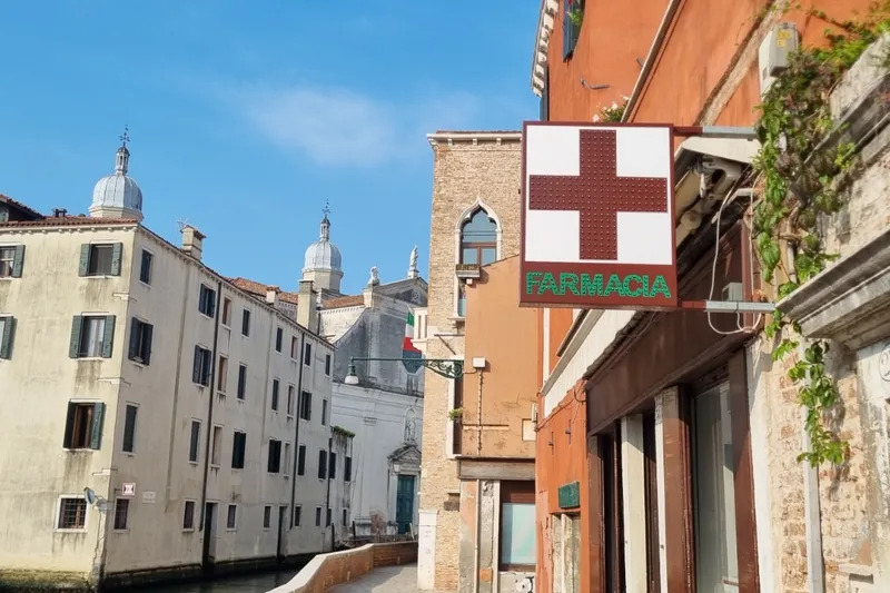Insegna a bandiera FARMACIA su una calle di Venezia, accanto al canale